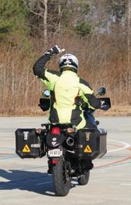 Motorcyclist with their left arm raised above their head and pointing right