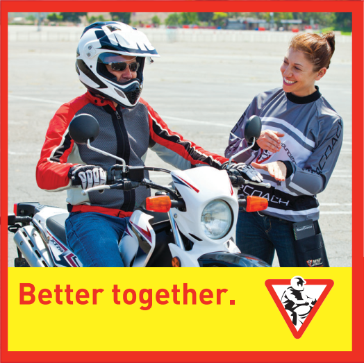 A person in a "coach" uniform standing and smiling at another person on a stopped motorcycle, wearing a motorcycle helmet.