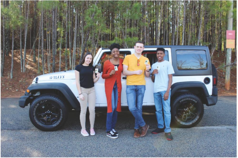 Four young people, each holding up an ID card or license, stand in front of a parked car. 