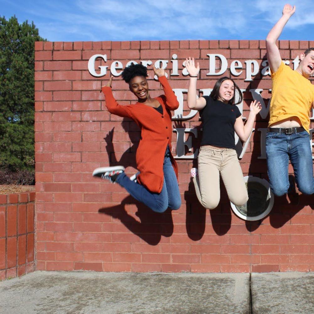 A group of four teenagers jumping for joy in front of the Georgia Department of Driver Services sign