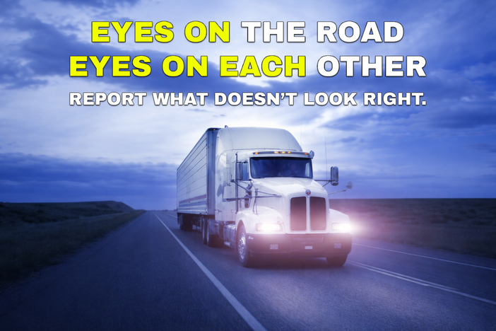 A commercial truck driving along the road with the words "Eyes on the road eyes on each other report what doesn't look right" displayed above the truck.